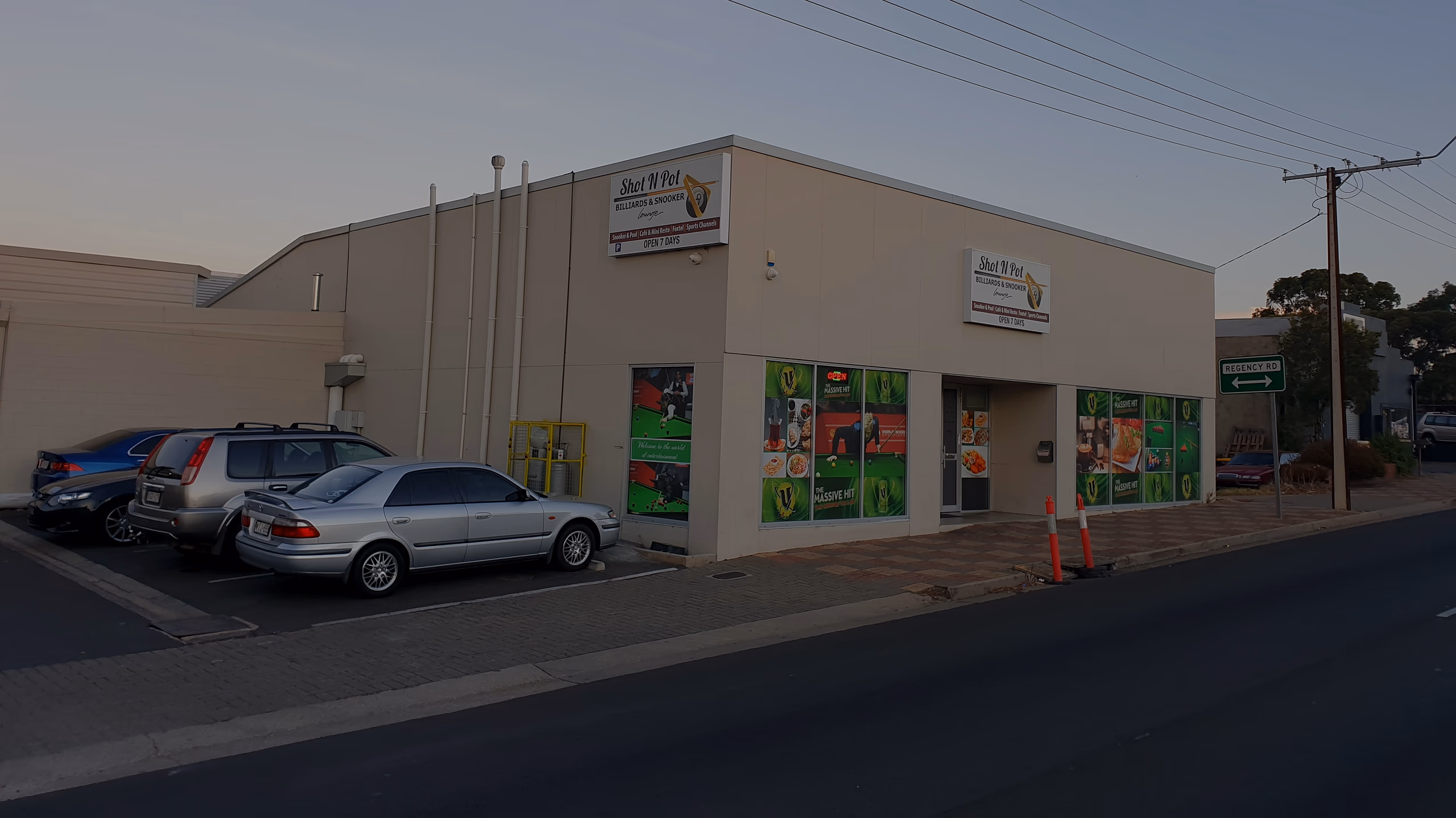 The club's cream building on the corner of Main North Road at dusk, two Shot N Pot signs, cars in the front car park.