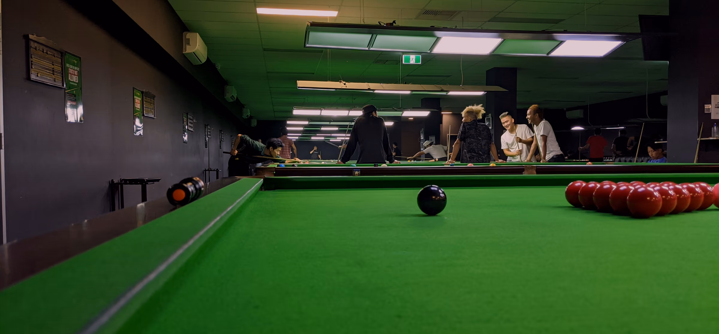 A rack of reds seen low along the cushion rail, the cloth running away to the far end of the table and the rest of the room out of focus behind.